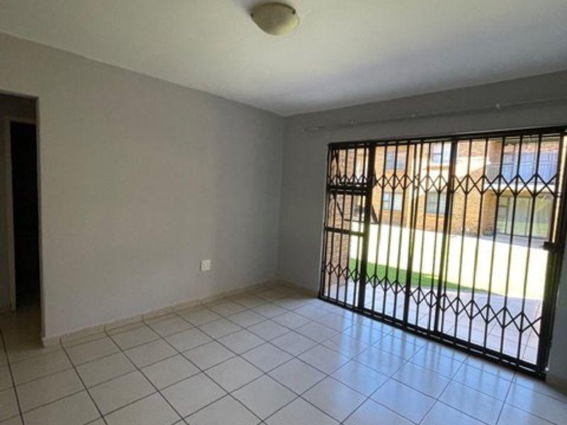 An empty living room featuring tiled flooring, a ceiling light fixture, and a sliding glass door with a security gate leading to the exterior.