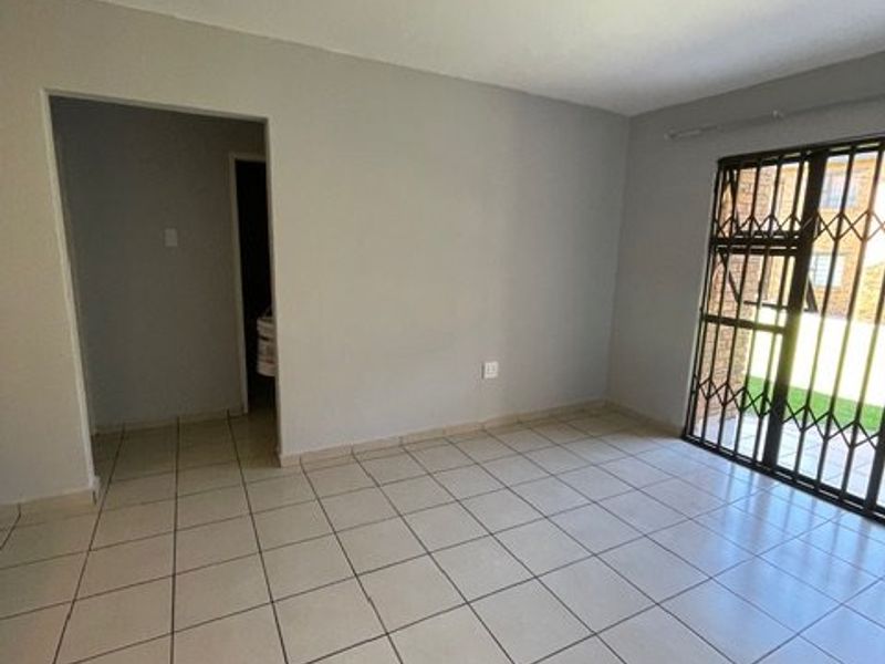 An empty, neutrally painted living room featuring ceramic floor tiles and a security gate leading to the exterior.