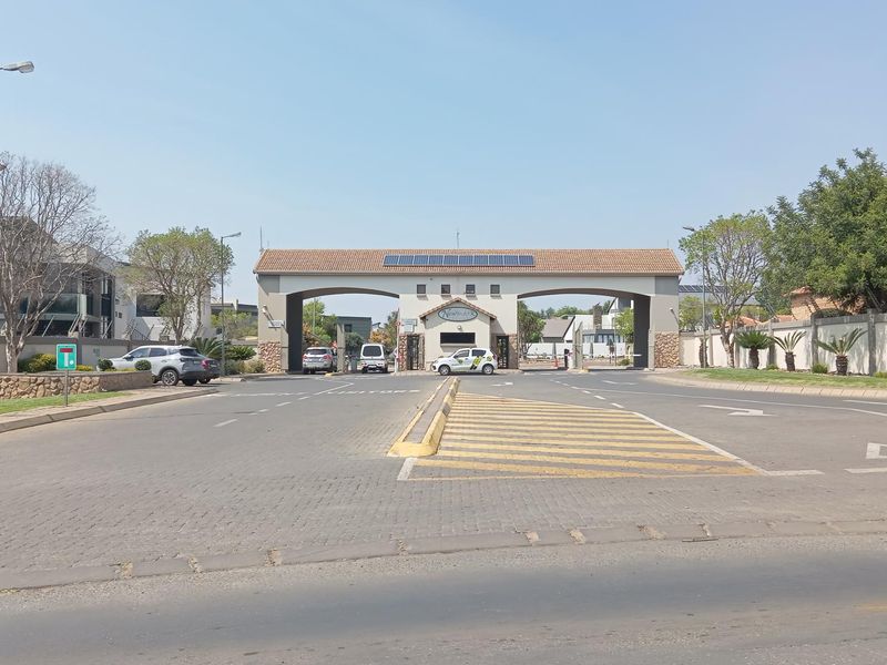View of the secure entrance gatehouse to the residential estate, featuring paved access roads and perimeter walling.