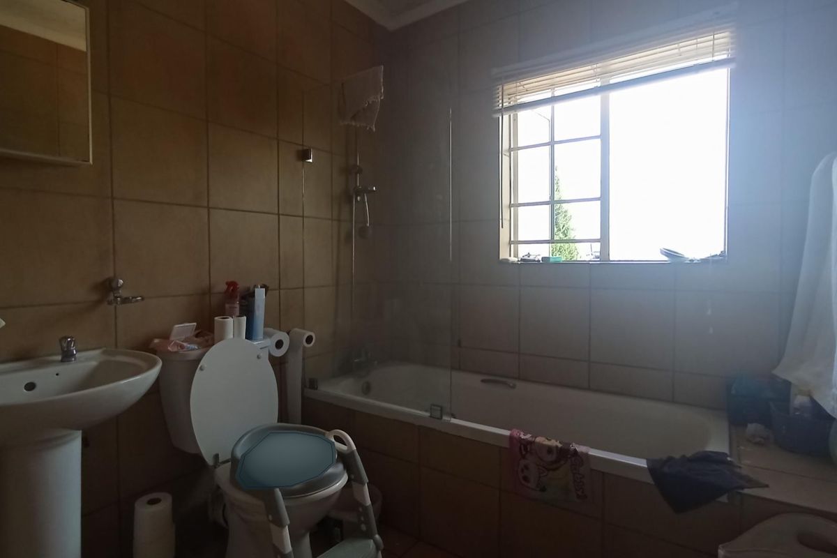 A functional bathroom featuring a pedestal basin, toilet, and a bathtub with a glass shower screen, finished with full-height wall tiling.