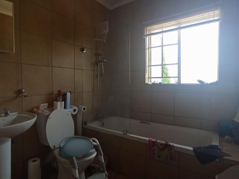 A functional bathroom featuring a pedestal basin, toilet, and a bathtub with a glass shower screen, finished with full-height wall tiling.