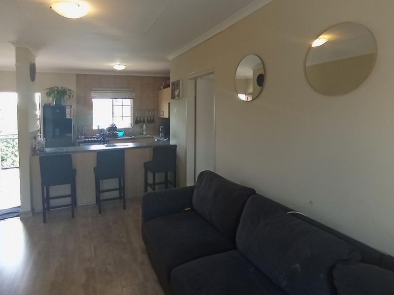 An open-plan living and kitchen area featuring a breakfast bar, laminate flooring, and neutral wall finishes, providing a functional and connected living space.