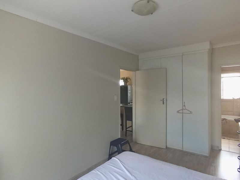 A functional bedroom featuring built-in wardrobes, laminate flooring, and direct access to an adjoining bathroom.