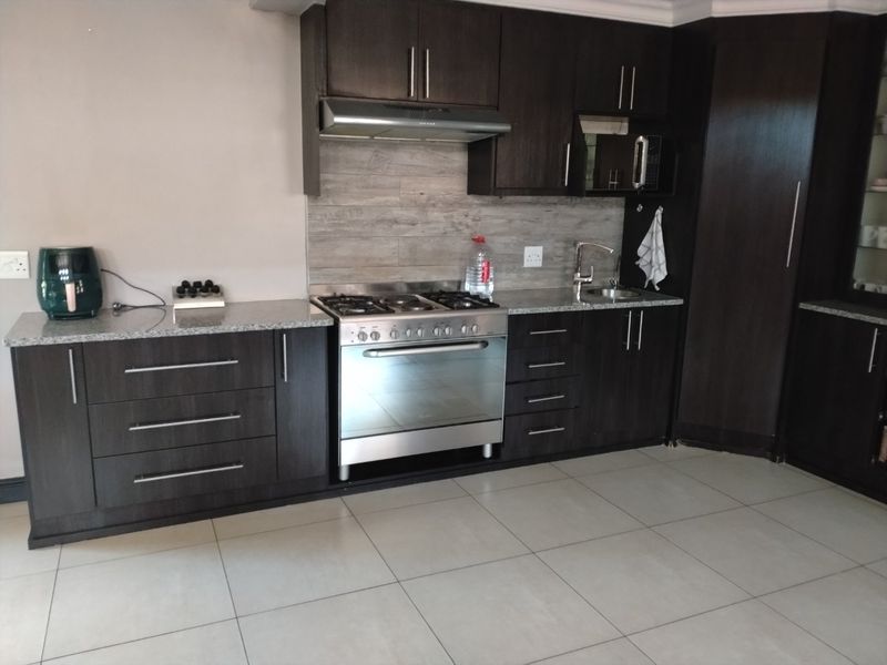 Modern kitchen featuring dark wood cabinetry, granite countertops, a gas stove with extractor fan, and a tiled backsplash with neutral floor tiles.
