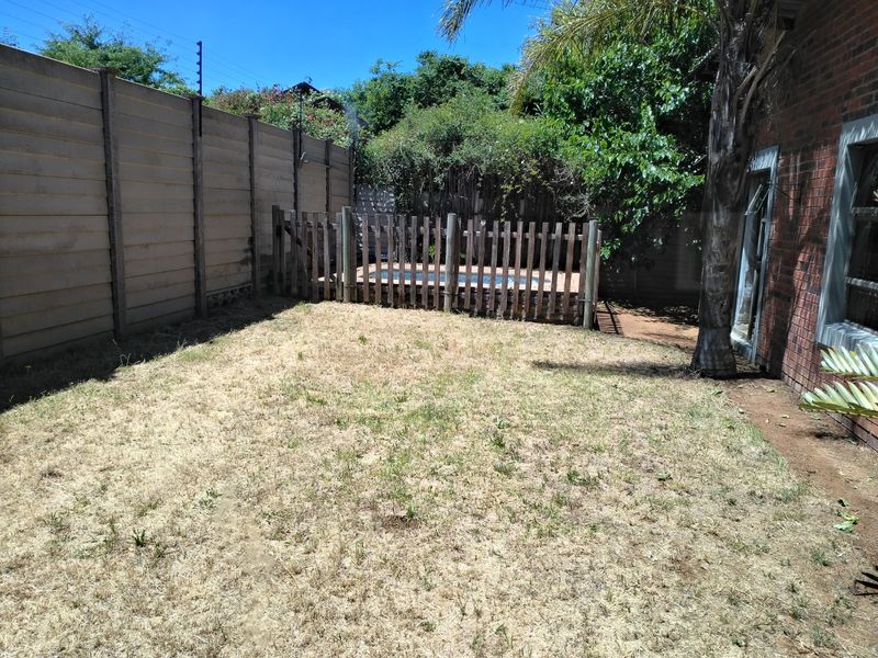 A rear garden area featuring a swimming pool enclosed by a wooden safety fence, bordered by a precast concrete wall with electric fencing.