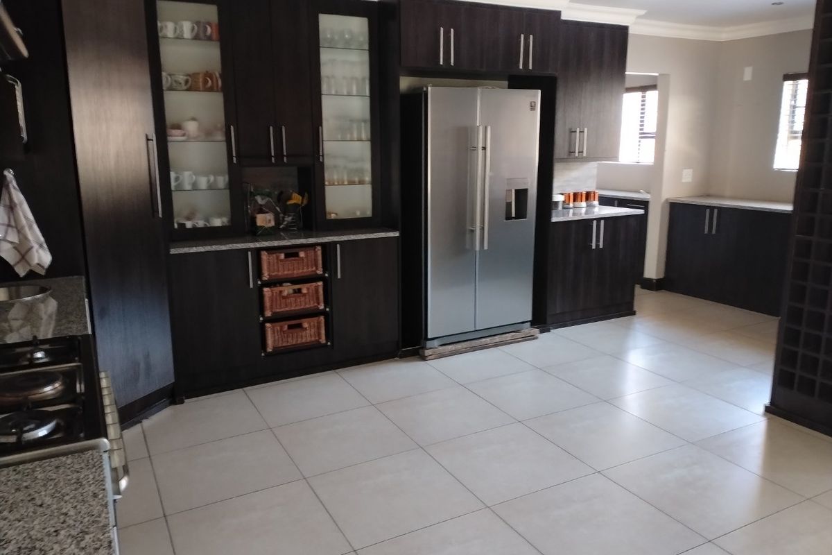 Spacious kitchen featuring dark wood cabinetry, granite countertops, built-in glass display units, and a dedicated wine rack, complemented by neutral ceramic floor tiles.