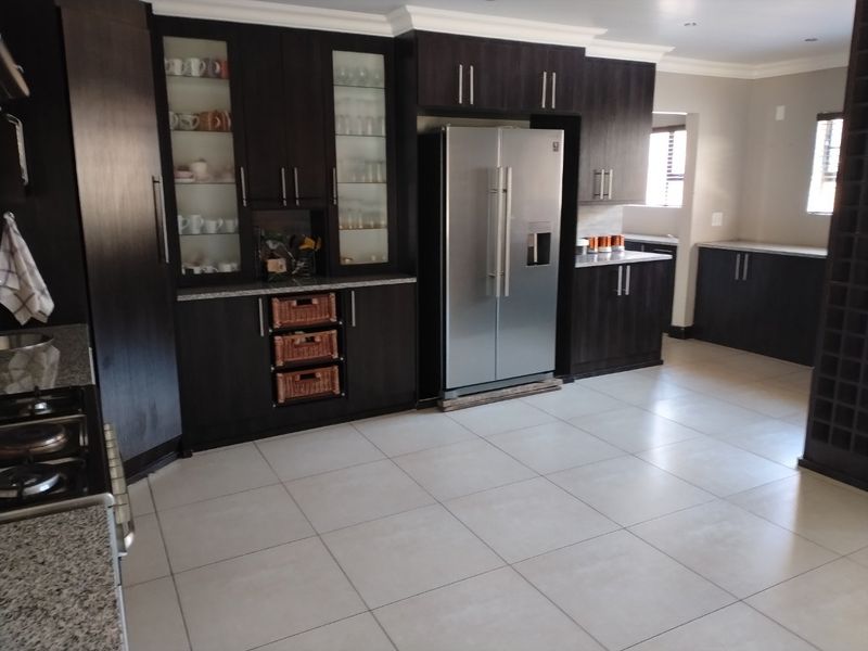 Spacious kitchen featuring dark wood cabinetry, granite countertops, built-in glass display units, and a dedicated wine rack, complemented by neutral ceramic floor tiles.
