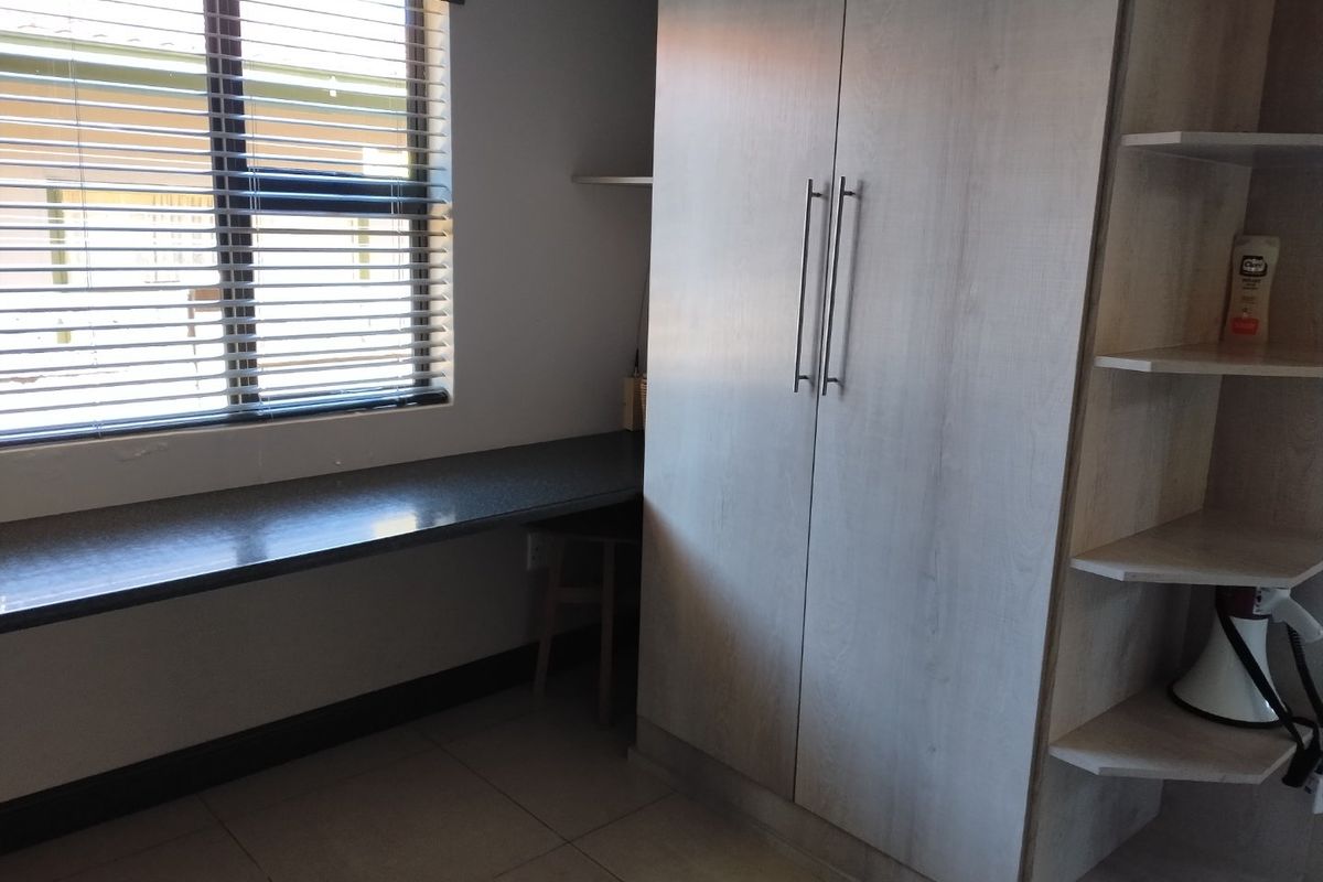 A functional bedroom featuring a built-in wardrobe, integrated desk space, open shelving, and tiled flooring with venetian blinds.