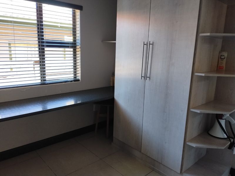 A functional bedroom featuring a built-in wardrobe, integrated desk space, open shelving, and tiled flooring with venetian blinds.