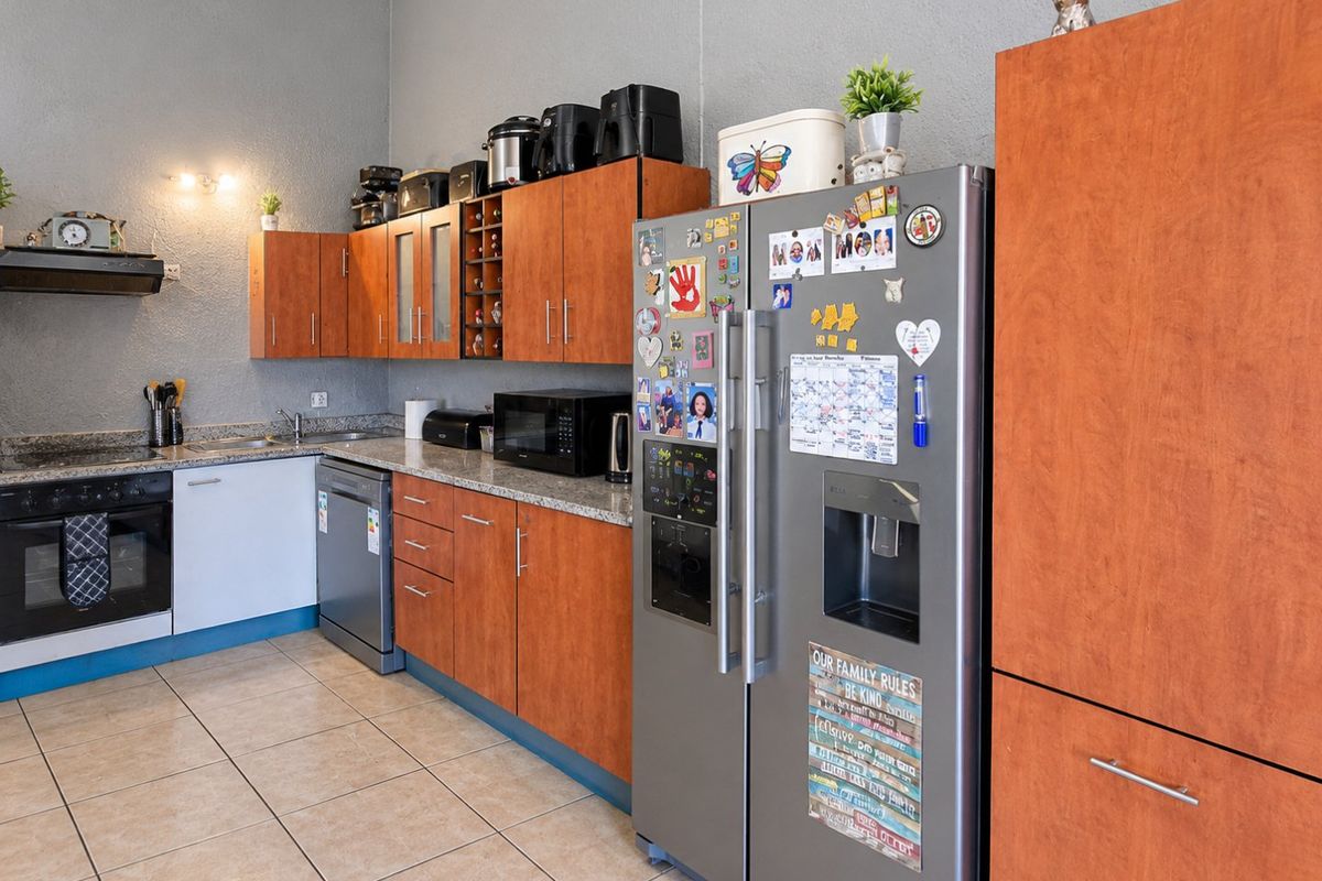 Functional kitchen featuring wood-finish cabinetry, granite countertops, integrated oven, hob, and extractor fan with tiled flooring.