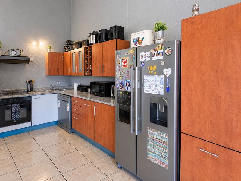 Functional kitchen featuring wood-finish cabinetry, granite countertops, integrated oven, hob, and extractor fan with tiled flooring.