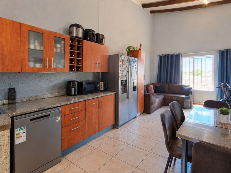Open-plan kitchen and living area featuring granite countertops, wood-finish cabinetry, tiled flooring, and exposed timber ceiling beams, creating a functional and connected living space.