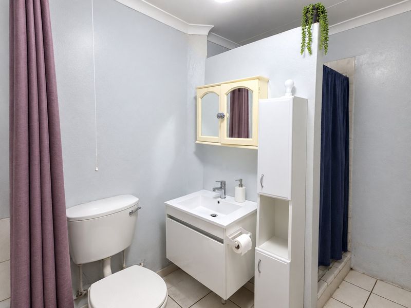 A functional bathroom featuring a vanity basin, toilet, and a shower cubicle with a privacy curtain, finished with tiled flooring.