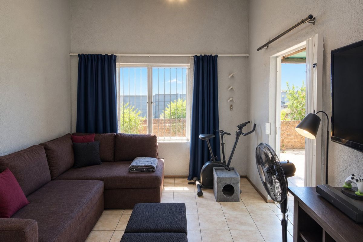 A functional living room featuring tiled flooring, a large window with security bars, and direct access to an outdoor area through a sliding door.