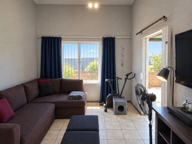 A functional living room featuring tiled flooring, a large window with security bars, and direct access to an outdoor area through a sliding door.