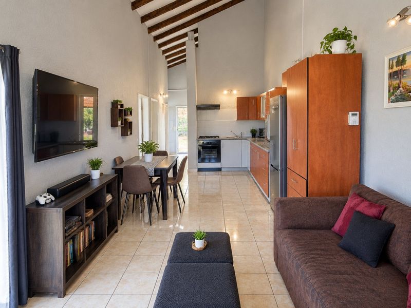 Open-plan living and kitchen area featuring high vaulted ceilings with exposed timber beams, tiled flooring, and functional built-in cabinetry.