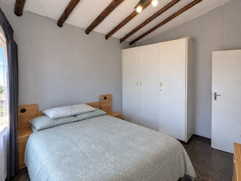 A bedroom featuring exposed timber ceiling beams, a built-in wardrobe, and tiled flooring.