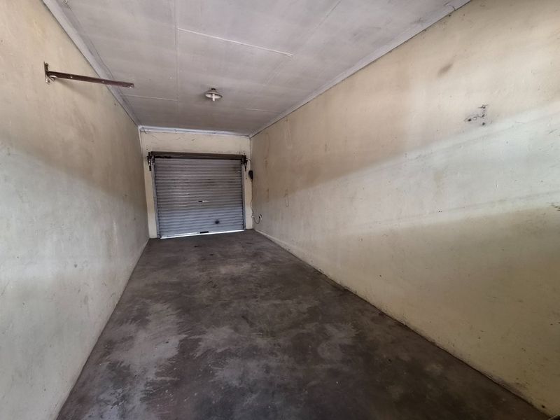 An empty single-car garage featuring a roller shutter door, concrete flooring, and basic lighting, requiring cosmetic updates to the wall finishes.