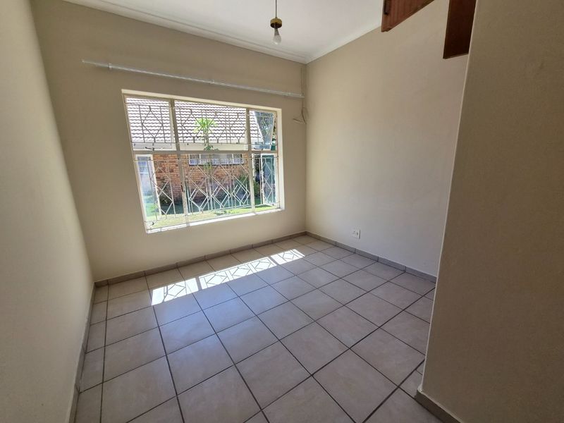 An empty bedroom featuring tiled flooring, a large window with security bars, and neutral wall finishes, ready for personalization.