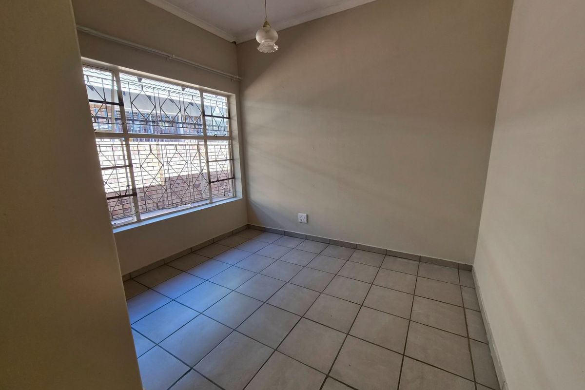 An empty bedroom featuring neutral tiled flooring, a large window with security bars, and a simple pendant light fixture.