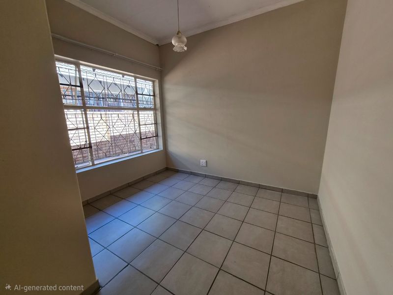 An empty bedroom featuring neutral tiled flooring, a large window with security bars, and a simple pendant light fixture.
