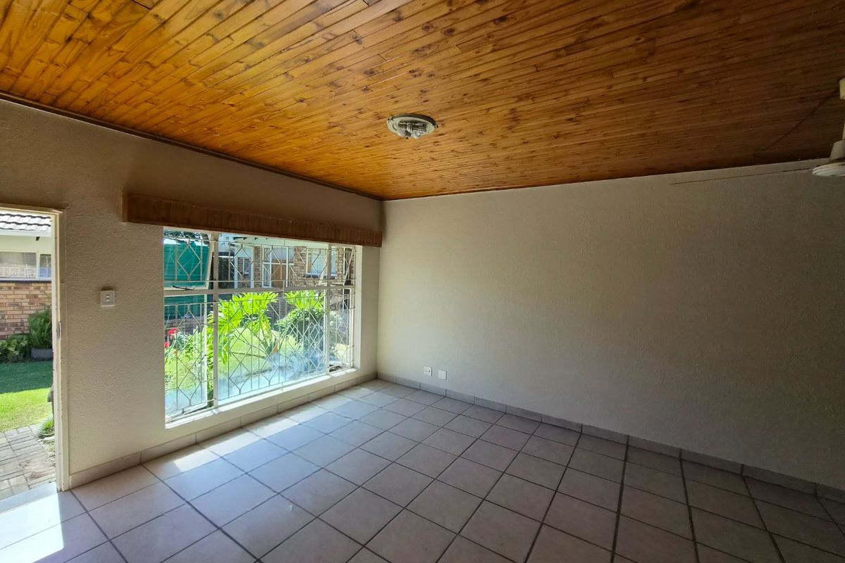 An empty living room featuring a warm timber tongue and groove ceiling, ceramic tiled flooring, and large windows with security bars.