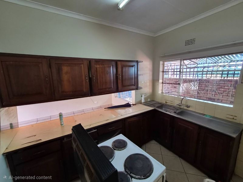 A dated kitchen featuring dark wooden cabinetry, laminate countertops, a stainless steel sink, and an electric stove, with security bars on the window.