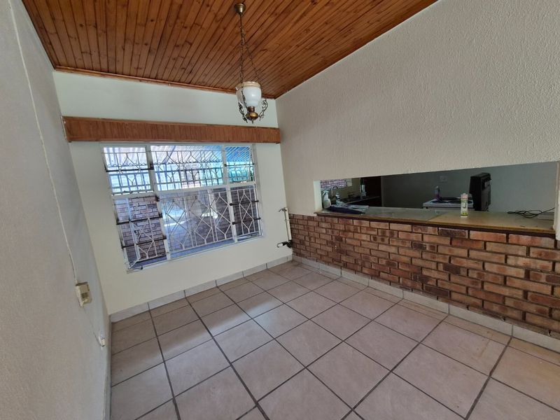 Open plan living area featuring tiled flooring, a timber ceiling, and a brick breakfast bar connecting to the kitchen space.