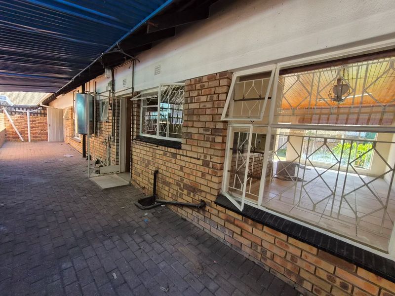 Rear exterior view of the townhouse featuring a paved walkway, brick facade, security bars on windows, and an external geyser installation.