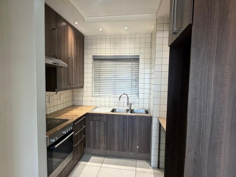 A modern, well-maintained kitchen featuring dark wood cabinetry, granite countertops, built-in appliances, and clean tiled finishes throughout.