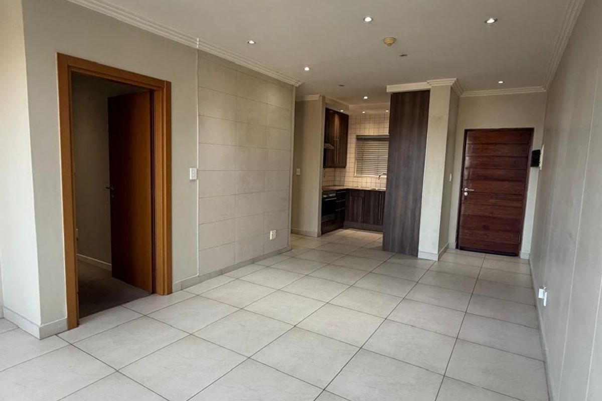 An open-plan living and kitchen area featuring neutral tiled flooring, recessed lighting, and modern kitchen cabinetry in a clean, vacant space.