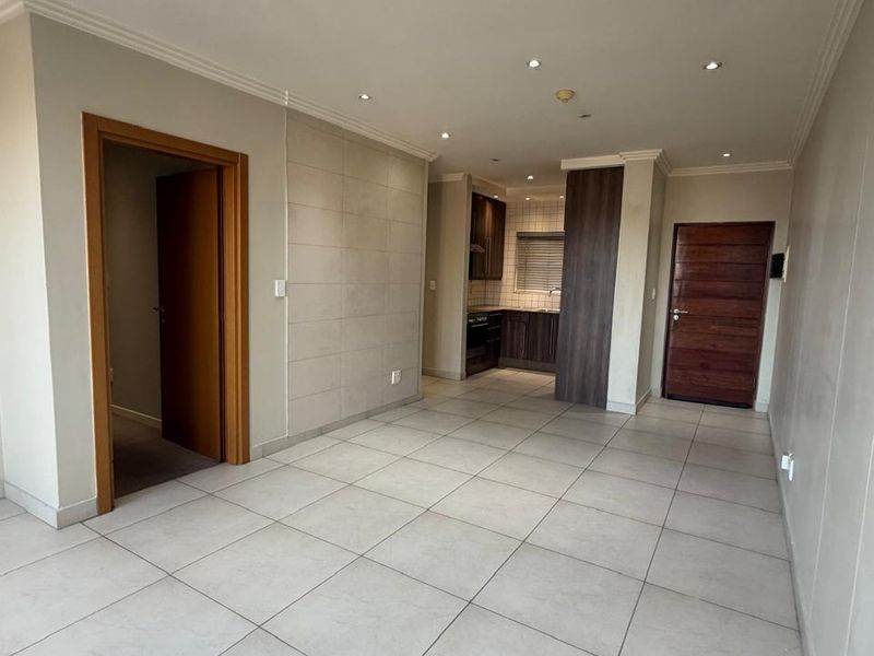 An open-plan living and kitchen area featuring neutral tiled flooring, recessed lighting, and modern kitchen cabinetry in a clean, vacant space.