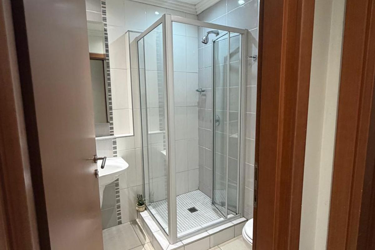 A clean and functional bathroom featuring a glass shower enclosure, wall-mounted basin, and neutral floor tiling with recessed lighting.
