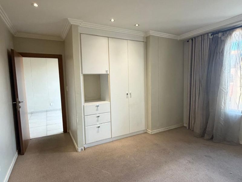 A spacious, empty bedroom featuring built-in cupboards, recessed downlighting, and neutral wall finishes, offering a blank canvas for personalization.