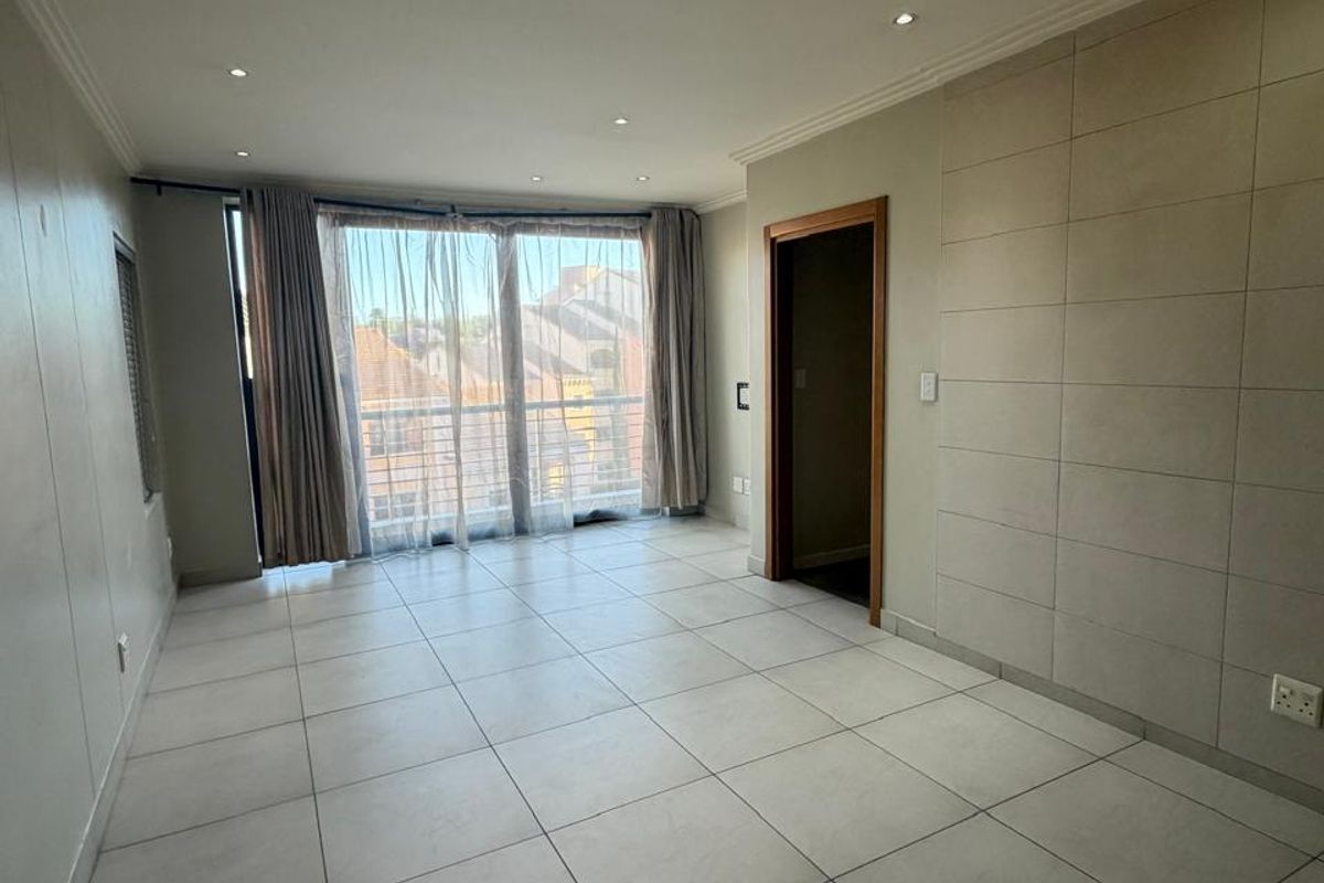 A bright, empty living room featuring modern tiled flooring, a tiled feature wall, and large sliding glass doors leading to a balcony.
