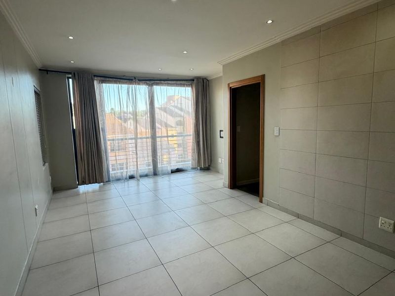 A bright, empty living room featuring modern tiled flooring, a tiled feature wall, and large sliding glass doors leading to a balcony.