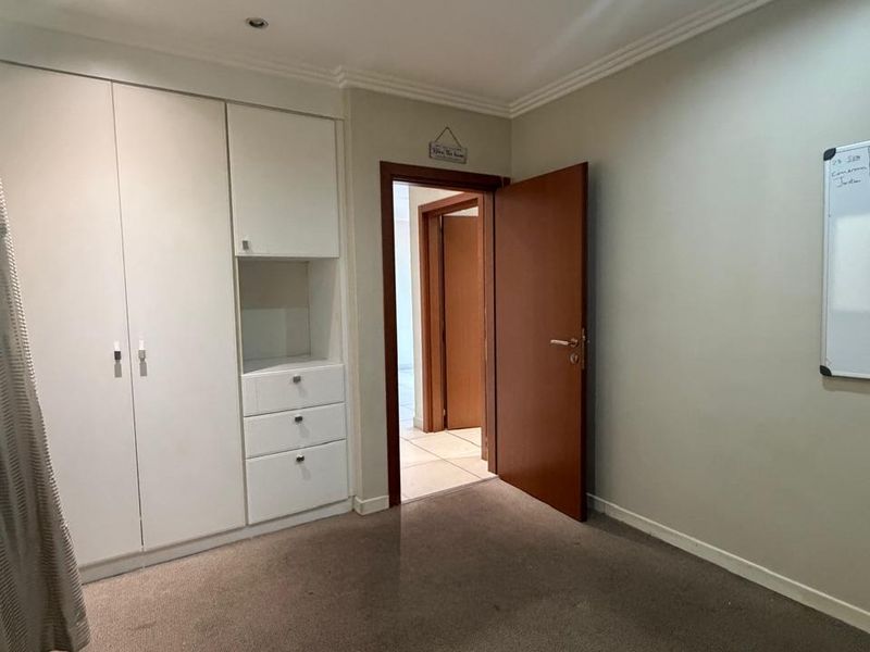 A clean, empty bedroom featuring built-in white cupboards, recessed downlighting, and neutral carpeting, offering a versatile space ready for personalization.