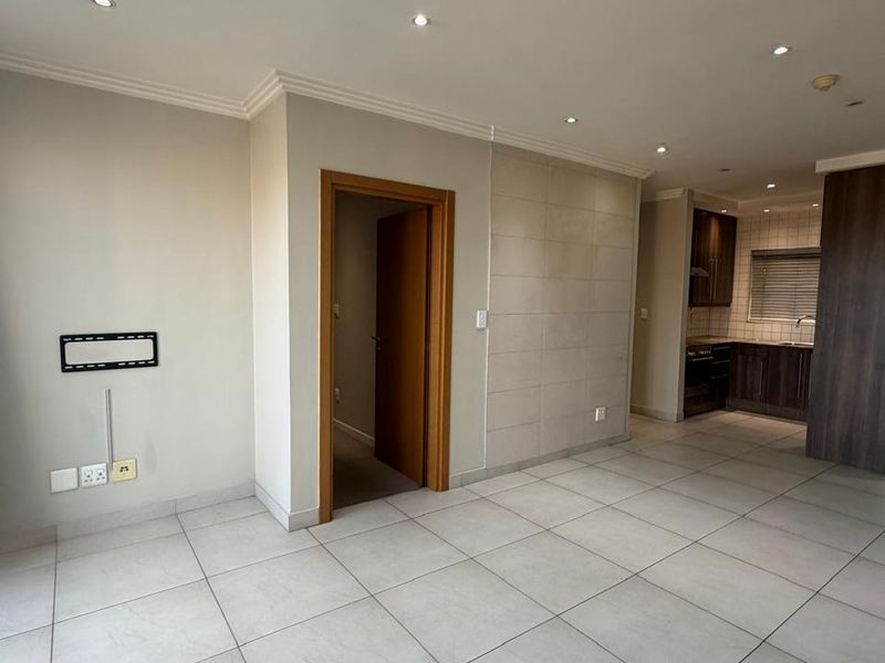 An open-plan living area featuring neutral tiled flooring, recessed lighting, and a modern kitchen with built-in cabinetry and a tiled feature wall.