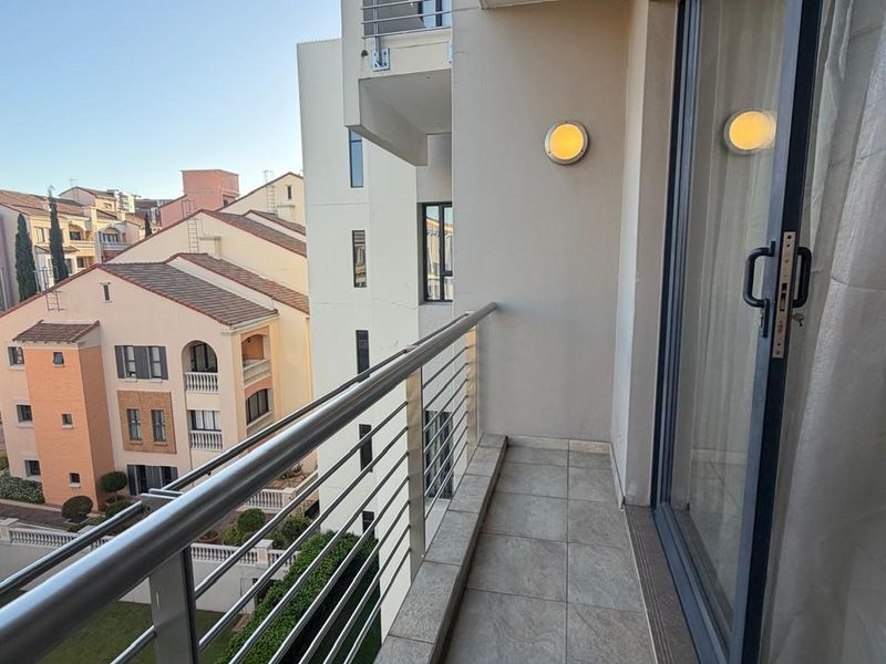 A clean, modern balcony featuring tiled flooring, a stainless steel balustrade, and a sliding glass door, offering views of the surrounding apartment complex.