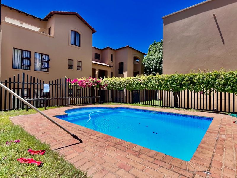 A communal swimming pool area featuring brick paving and metal perimeter fencing, set within an apartment complex courtyard.