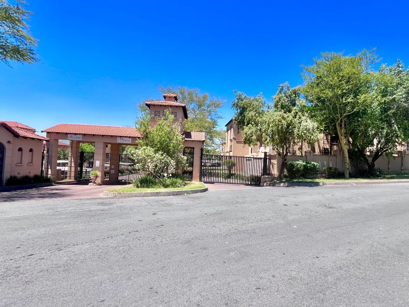A view of the secure gated entrance to the apartment complex, featuring a guard house, perimeter walling, and paved access.