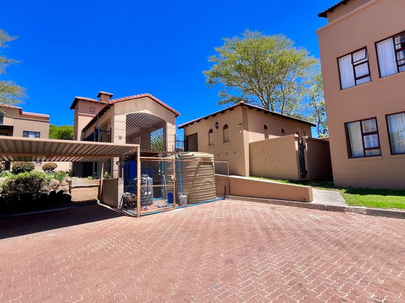 Exterior view of an apartment complex featuring a paved driveway, covered carport, and a water storage tank installation.