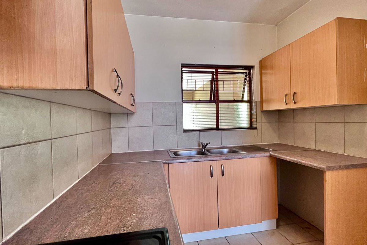 A functional kitchen featuring laminate cabinetry, double bowl stainless steel sink, tiled splashback, and tiled flooring, offering a clean canvas for potential updates.