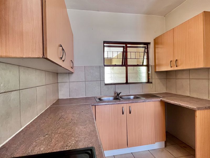 A functional kitchen featuring laminate cabinetry, double bowl stainless steel sink, tiled splashback, and tiled flooring, offering a clean canvas for potential updates.