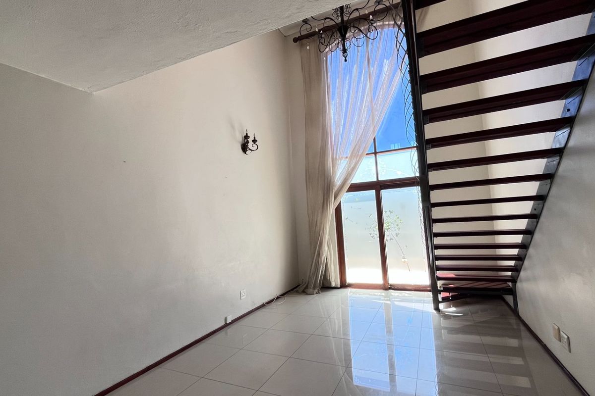 Bright living area featuring high ceilings, large floor-to-ceiling windows, tiled flooring, and an open-tread staircase leading to the upper level.
