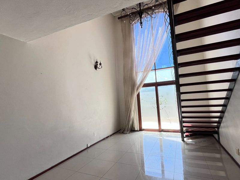 Bright living area featuring high ceilings, large floor-to-ceiling windows, tiled flooring, and an open-tread staircase leading to the upper level.