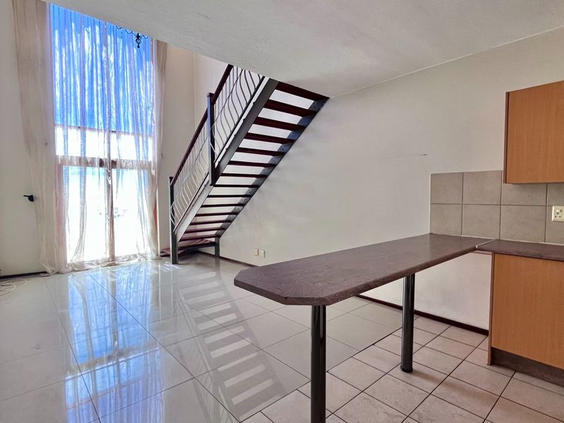 Open-plan living area featuring a staircase, tiled flooring, and a functional kitchen with built-in cabinetry and a breakfast bar.