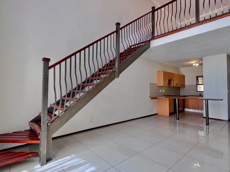Open plan living area featuring a prominent staircase with metal balustrade, tiled flooring, and a functional kitchen space with built-in cabinetry.