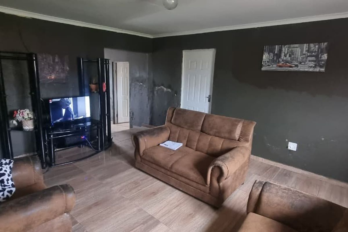 A living room featuring tiled flooring and coving, currently showing significant signs of wall dampness and surface finish deterioration requiring maintenance.