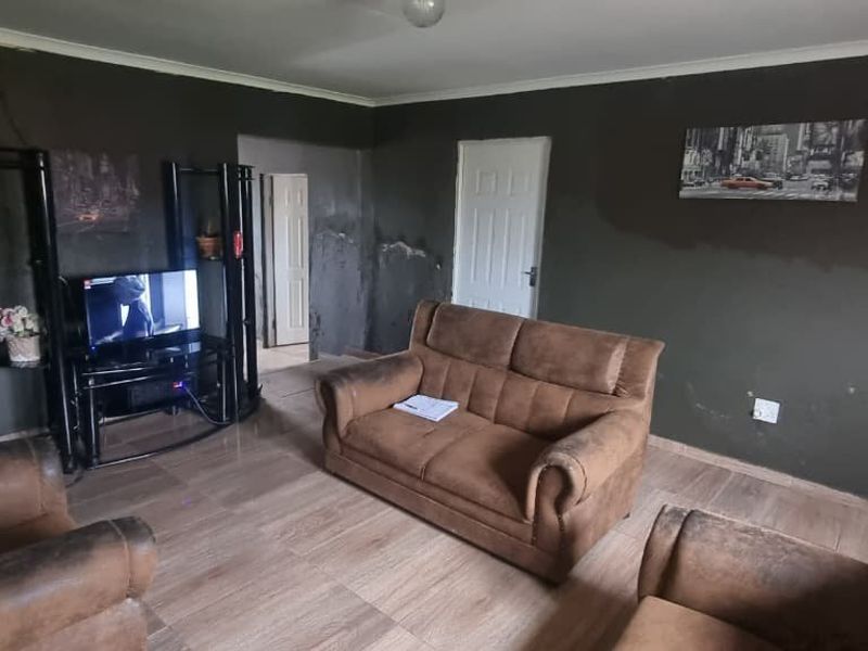 A living room featuring tiled flooring and coving, currently showing significant signs of wall dampness and surface finish deterioration requiring maintenance.